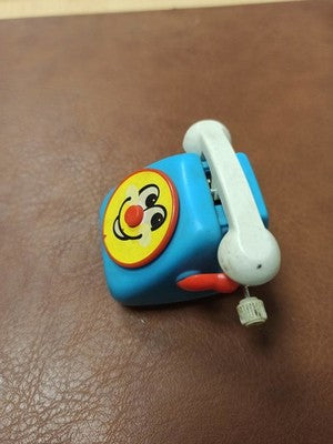 Téléphone jouet vintage Tomy 1978 bleu à remontoir, visage souriant rétro