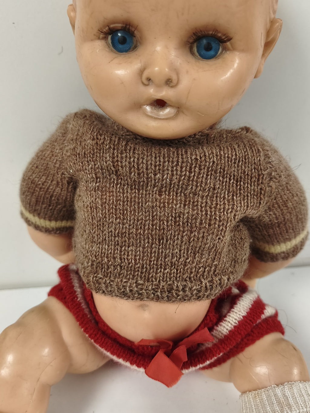 Poupée ancienne à yeux bleus, corps articulé, tenue tricotée brune