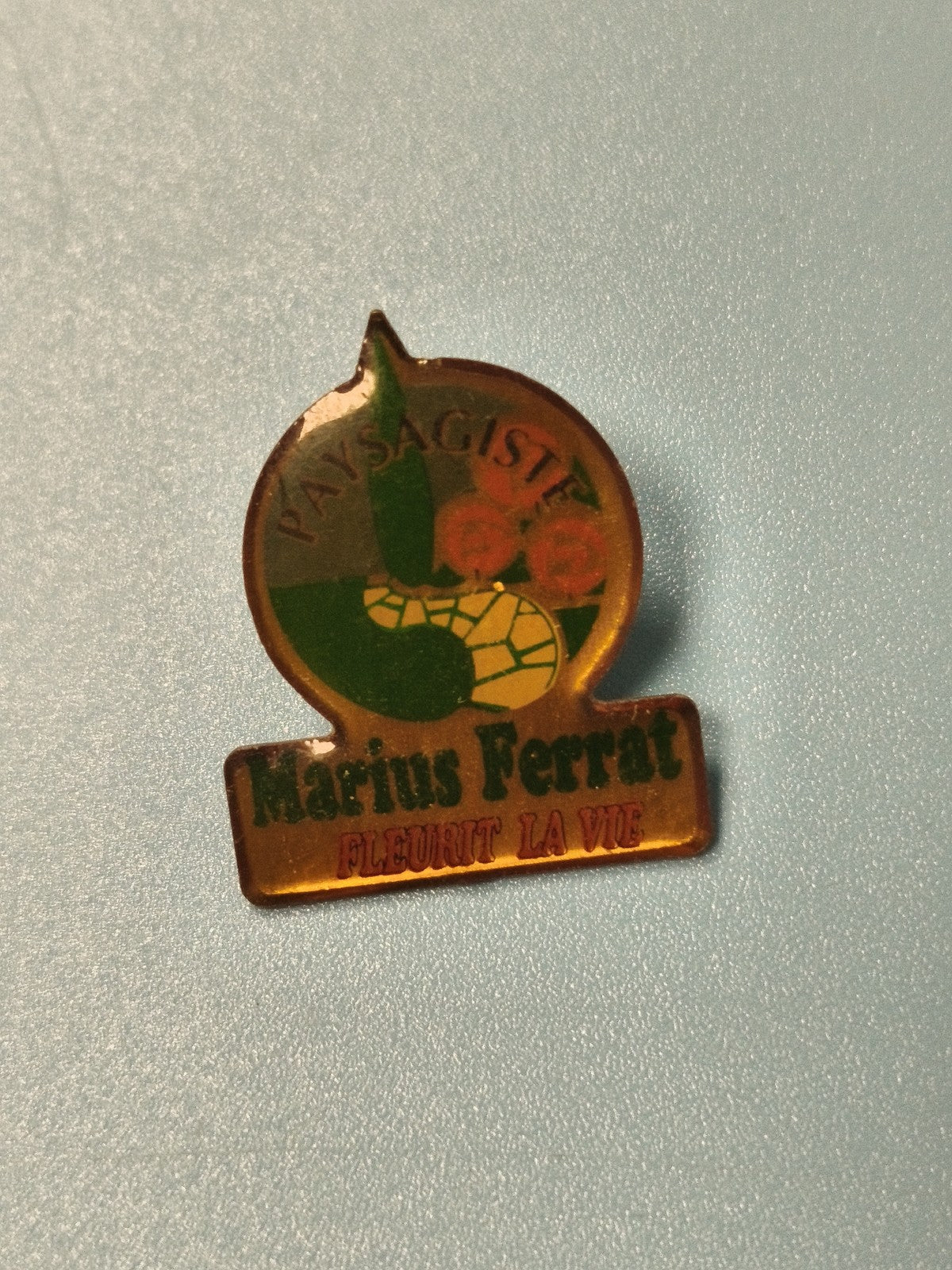 Vintage pin's publicitaire Marius Ferrat paysagiste, logo vert orange rétro
