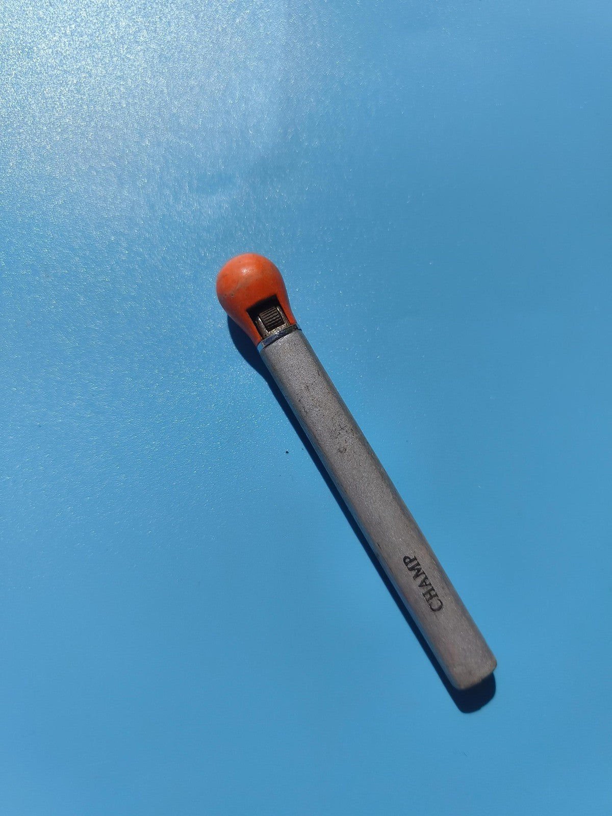 Ancien briquet publicitaire CHAMP, métal gris et tête orange, à restaurer