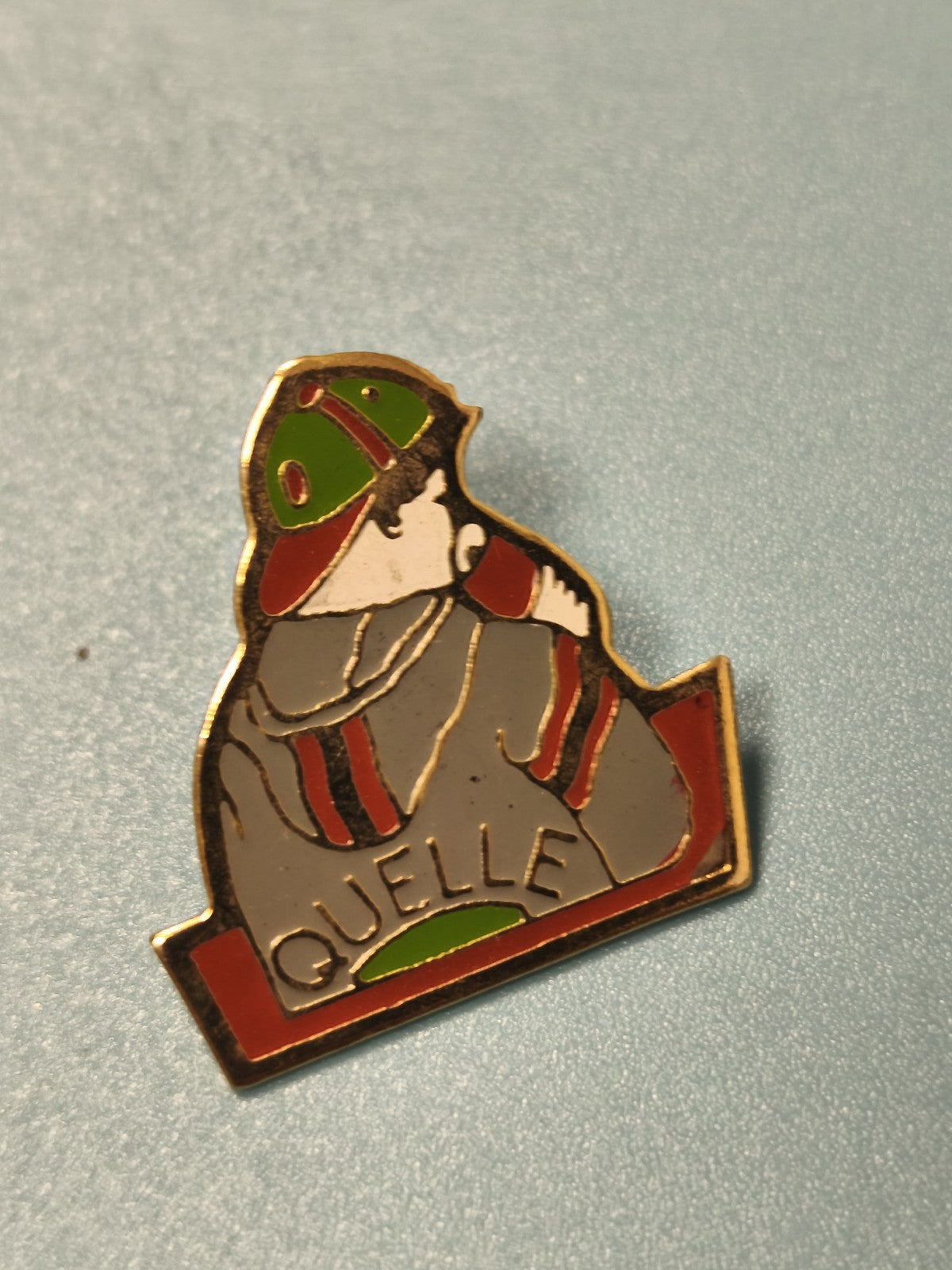 Vintage pin's publicitaire QUELLE émaillé, personnage casquette verte rouge