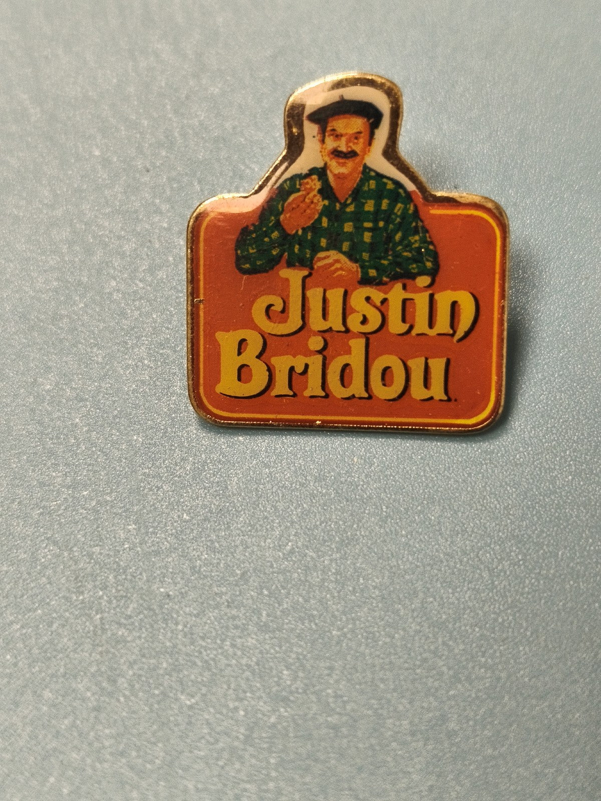 Pin's vintage Justin Bridou publicitaire, fond orange, personnage illustré, coll